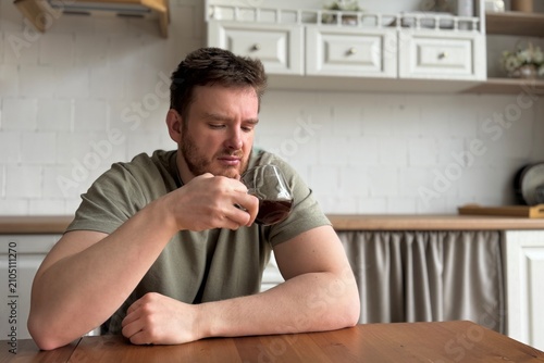 Fotografie man drinking coffee and suffer kitchen setting with wooden table and ceramic pitcher, daily life scene with green shirt and brown wooden table, close-up view of man enjoying coffee in home