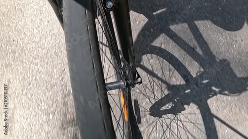 Bicycle fork and wheel close-up with the rider's shadow stretching across a sunlit road, capturing steady forward motion on a countryside ride.