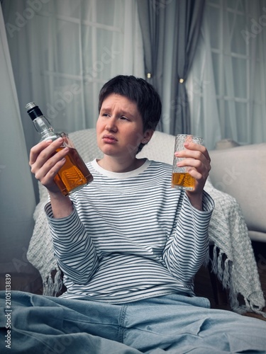 concerned woman holding alcohol bottle and glass in living room with sofa, curtains, and blanket period period period period period period period period period period period period period.