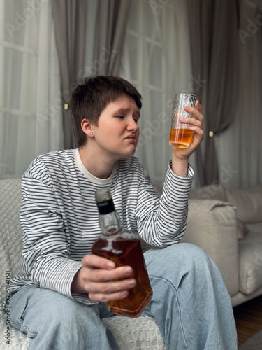 person casually holding bottle and glass in indoor setting with curtains and furniture, everyday life scene, casual mood, gray and white colors, textile and plastic materials, front view.