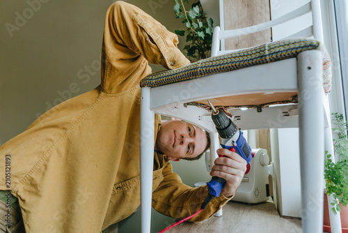 Smiling man using drill on chair at home