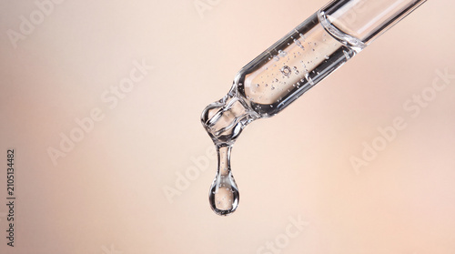 Dropper serum liquid droplet skincare pipette macro photo of clear droplet hanging from glass dropper beige background