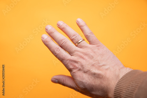 Schilderij op canvas Male hand with a golden ring on the yellow background.