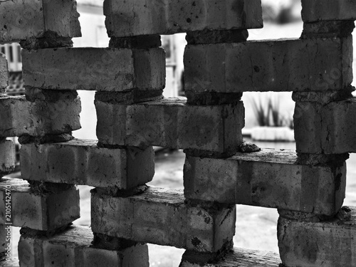 A close-up, black and white photograph of an ornamental brick wall with a hollow decorative pattern, showcasing geometric gaps, rustic textures, weathered mortar joints, and a unique architectural.