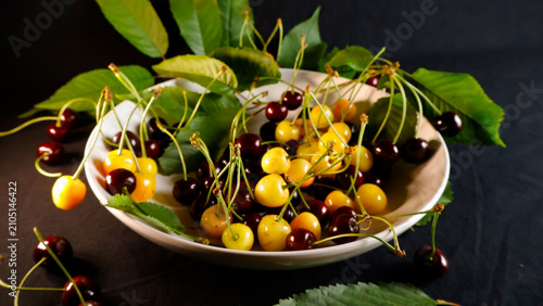 Fotografía Freshly picked red and yellow cherries, mingling with green leaves in a white bo