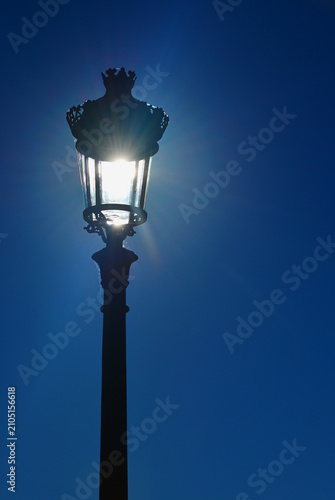 A street lamp lit by the sun in broad daylight, giving the impression that the bulb is on.