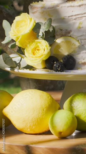 Vertical video: Panning camera showcasing tiered cake on pedestal in garden with lemon wedge, roses