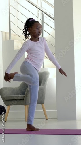 Vertical video: Practicing from arms-up kid in activewear balancing on purple mat home holding foot
