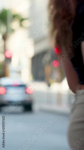Vertical video: Waiting woman black top tan bag at curb yellow pole watching light change to cross