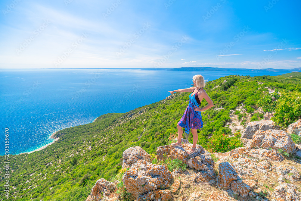 Obraz premium Woman in a colorful dress and hat enjoying the panoramic view of the historic Lubenice village on Sveti Ivan Lubenice Beach. A medieval settlement on Cres Island. Croatia of Cres Island in Croatia