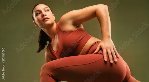 Fit woman in terracotta sportswear stretching and posing in a studio, showcasing strength, body positivity, and athletic wellness, isolated.