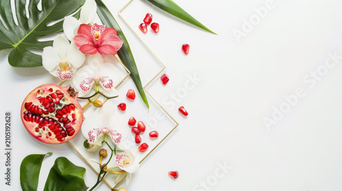 Elegant summer composition with pomegranate slices, orchid flowers and monstera leaves on white background with golden frame and place for text