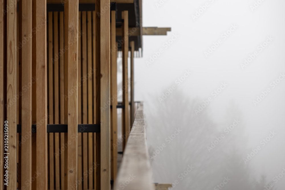 Naklejka premium A vertical wooden slat facade on a balcony overlooking a dense fog, reflecting a minimalist architectural design that evokes tranquility and serene connection to the mountain nature