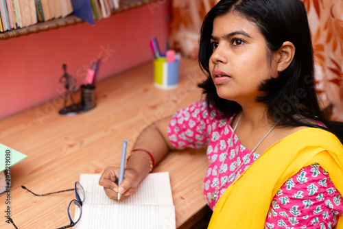 An Indian female writing on white notebook