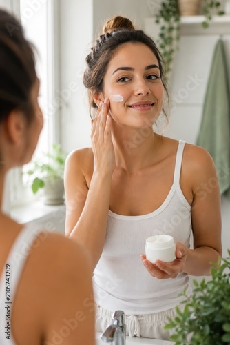 Young woman applying face cream in morning skincare routine at mirror