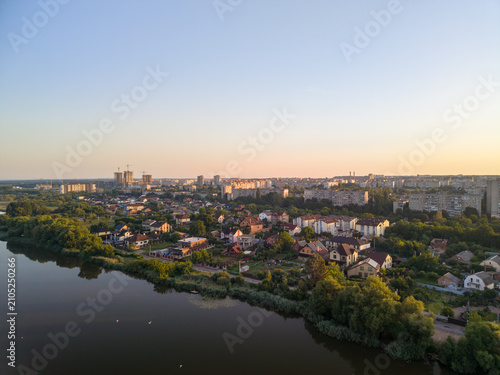 фотографія High angle drone perspective captures Vinnytsia city with a calm lake, residential buildings, and green trees under a soft sunrise sky at dawn