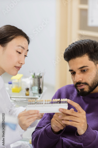 A dentist and patient examine a tooth shade guide to select the perfect color for dental work