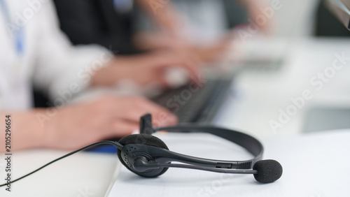 Close up of call center headset on desk with blurred agents typing