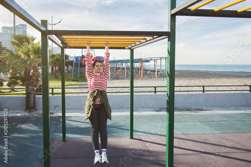Photography Woman hanging on monkey bars at outdoor fitness park near seaside, young adult p