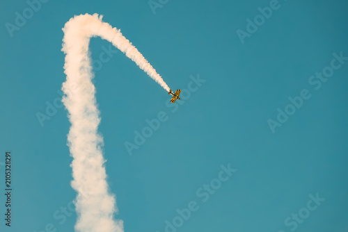Portugal Oeiras Air Show.  A stunt plane makes a loop in the sky while leaving a smoke trail. The scene shows a clear blue sky with the aircraft performing tricks for an audience below.