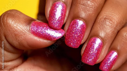 Hand with pink glitter nail polish on yellow background.