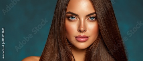 A beautiful woman with long brown hair and striking blue eyes gazes directly at the camera against a textured teal background.