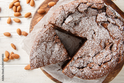 Italian Torta Caprese is a decadent, flourless cake made with dark chocolate and almonds closeup on the wooden board on the table. Horizontal top view from above