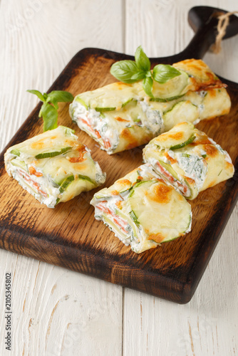 Baked Zucchini roll with cream cheese, herbs and salmon closeup on the wooden board on the table. Vertical