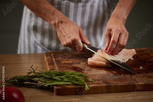 Chef slicing raw chicken breast on wooden board