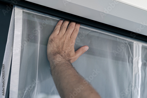 Obraz na płótnie Hand securing a white mosquito screen into the window frame, illustrating precise handwork in home tasks and maintenance