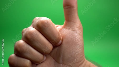 Male hand giving thumbs up gesture on green background.