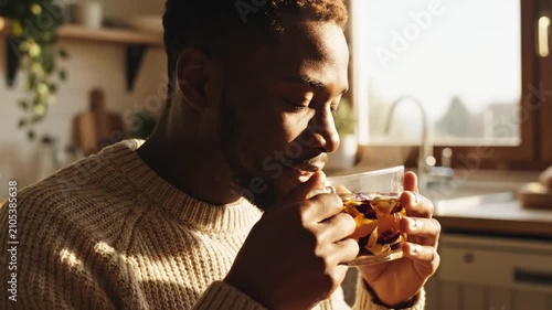 Man drinking herbal tea in sunlit morning kitchen.