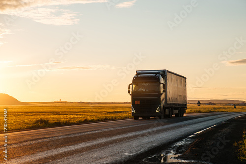 A truck is driving down the highway during an orange sunset, with the sun's rays