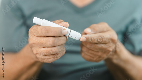 Photos Close-up of a senior adult using a lancet device for finger prick blood glucose testing at home