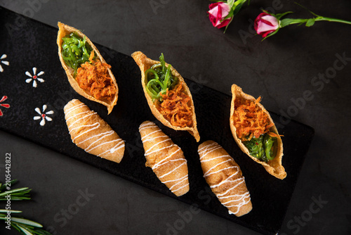 Japanese Style Appetizers with Inari Sushi and Sweet Pastry Rolls on Black Platter