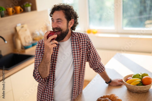 Happy man eating apple in kitchen enjoying healthy snack