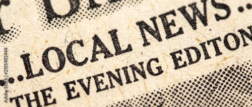 Close up of vintage newspaper print showing bold black text headline reading local news with evening edition typography on rough textured paper surface