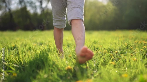 Person walking through field. Barefoot child walking in the grass at park. A kid is taking a walk in a park. An individual strolling lifestyle across a pasture.