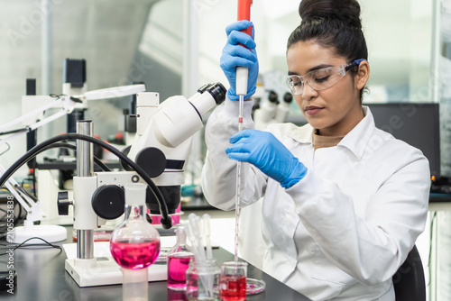 Woman scientist working with pipette and microscope in laboratory