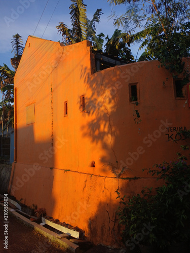 Bright orange weathered building exterior wall illuminated by warm golden hour sunlight featuring long shadows and rustic textures captured in a realistic outdoor setting during a beautiful late after