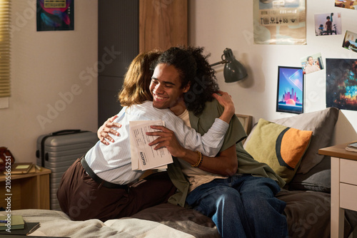 Canvas Print Young adult student hugging parent while holding accepted letter in bedroom, celebrating college admission and family support