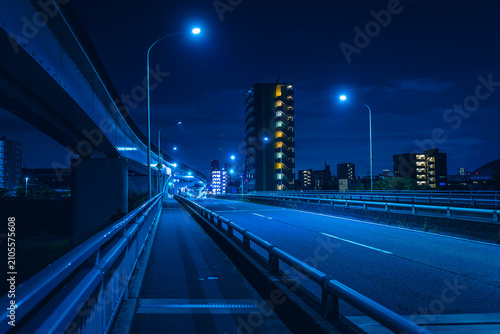 青い光に包まれた夜の橋と高架橋、遠くに輝くマンション群の都市風景