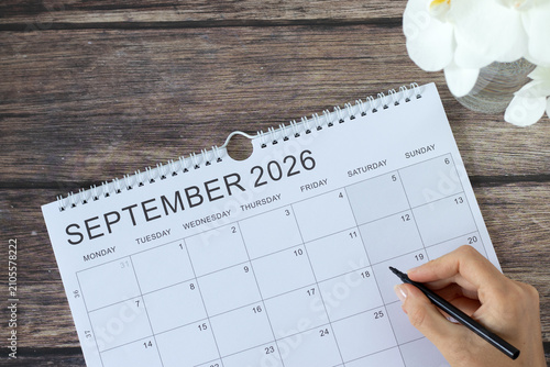 Hand holding a pen on top of September 2026 calendar.