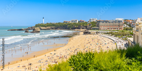 Panorama of the Grande Plage beach with the Hôtel du Palais and the distant Biarritz Lighthouse under a clear sky in Biarritz, France