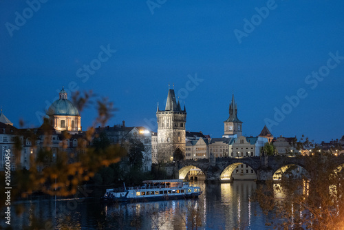Fotografia Illuminated charles bridge, old town bridge tower, and boat cruising vltava rive
