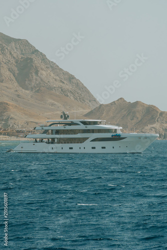 Large luxury yacht sailing on open water near arid coastline mountains promoting travel and leisure