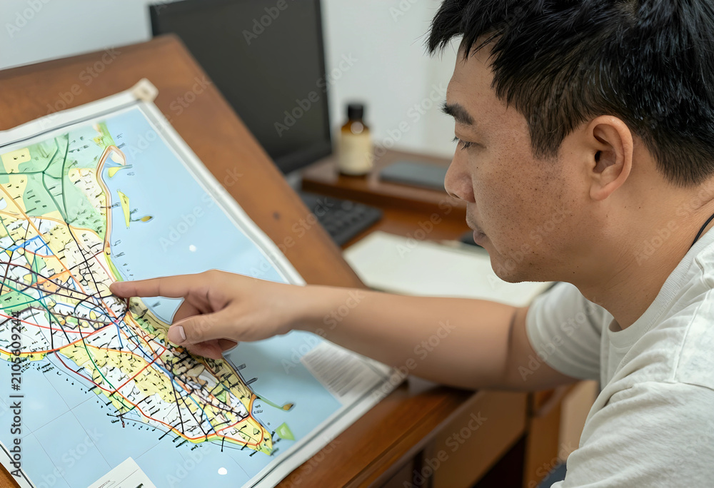 Naklejka premium Asian man pointing at a paper map, travel planning and navigation, route finding and destination search, close up