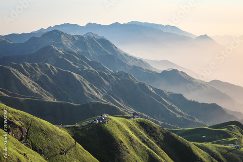 Fotografie Misty green mountain ridges with hilltop camp and winding path at sunrise