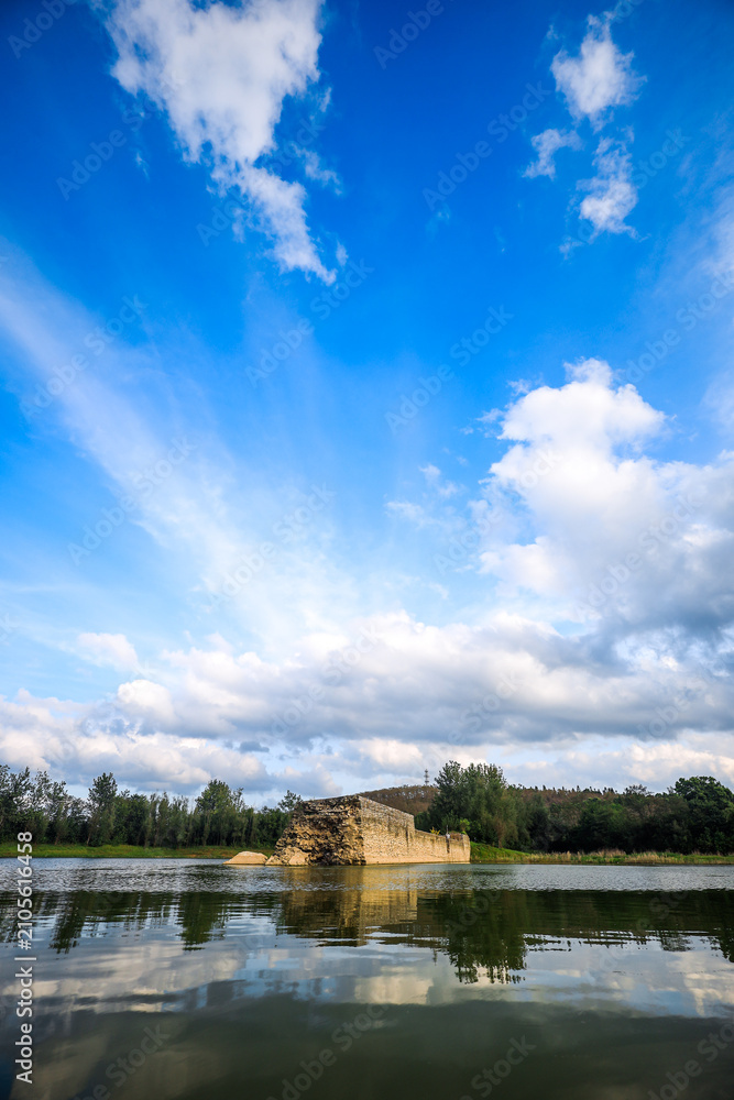 Fototapeta premium Stone Ruin by Calm Lake Under a Dramatic Blue Sky