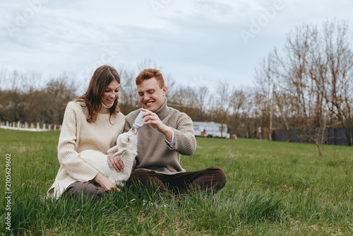 Fotografie Cheerful couple outdoors, interacting with a friendly goat kid, sitting on grass